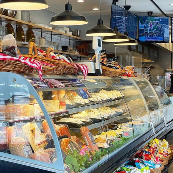 A deli display case filled with various meats, cheeses, and salads at The Bagels.