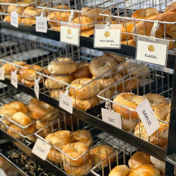 Multiple wire baskets filled with various bagels, including cheddar jalapeno, bialy, mini, flagel, onion, salt, garlic, and sesame.