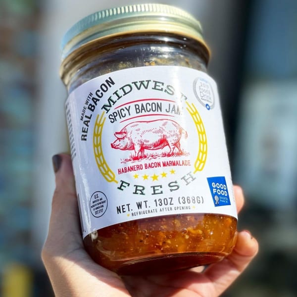 Hand holding a jar of Midwest Spicy Bacon Jam with a pig illustration on the label.