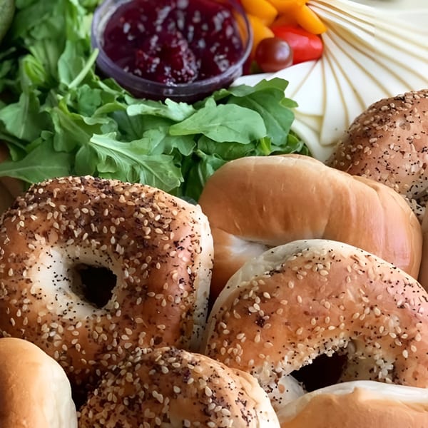 Assortment of bagels, including everything bagels, with a side of jam and fresh greens.