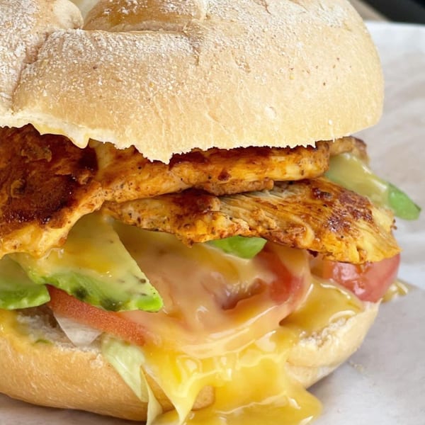 A bagel sandwich with grilled chicken, melted cheese, avocado, tomato, and lettuce.