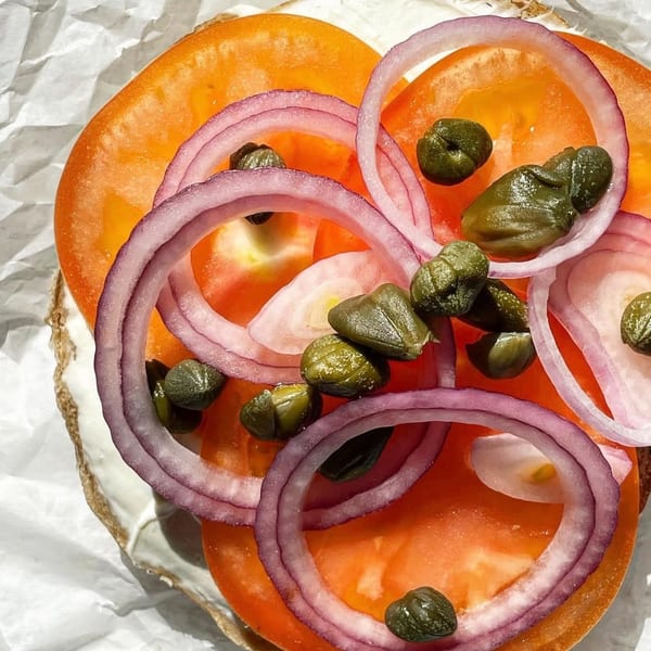 Close-up of a bagel with cream cheese, sliced tomatoes, red onions, and capers.