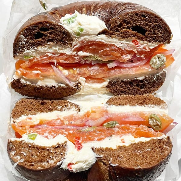 A dark bagel from The Bagels, sliced in half, filled with cream cheese, salmon, and capers.