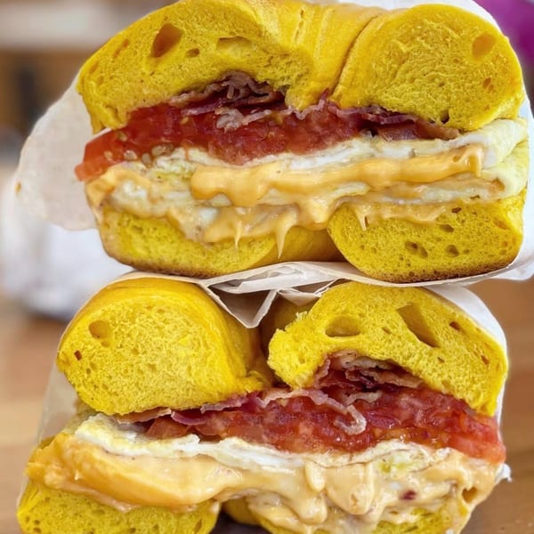 Two stacked, golden bagels from The Bagels, filled with bacon, egg, cheese, and tomato.